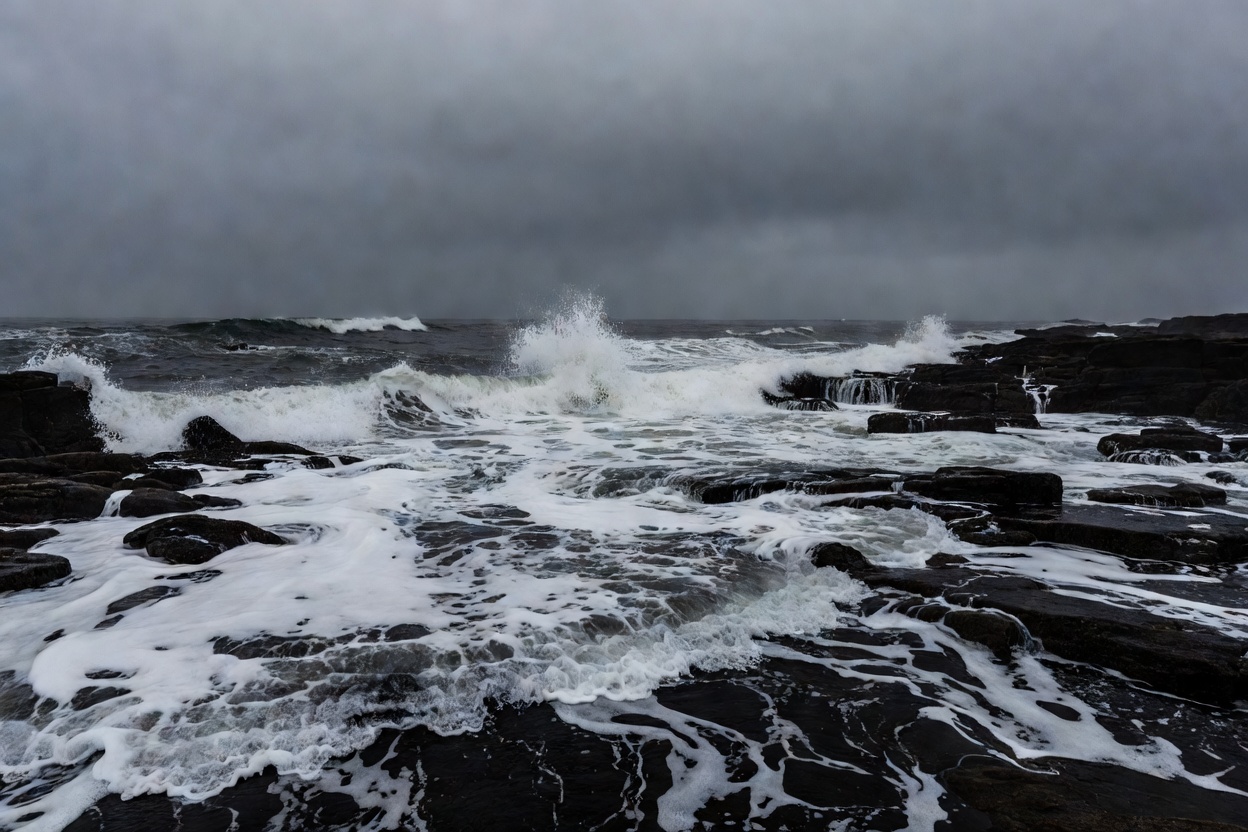 Waves washing over dark rocks on an incoming tide beneath a heavy grey sky