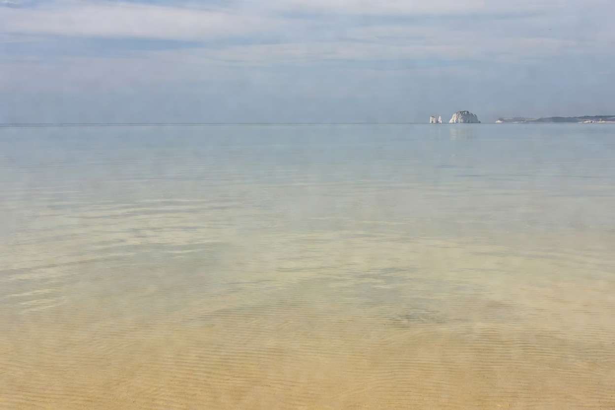 Calm, shallow water at Knoll Beach in Studland Bay with Old Harry Rocks faint in the distance